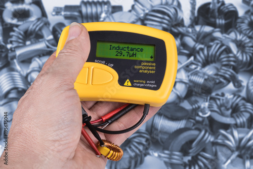 Detail of hand with digital meter of electric passive components. Technical expert when testing inductance of coils using the measuring instrument. Idea of professional work in electronics industry. photo