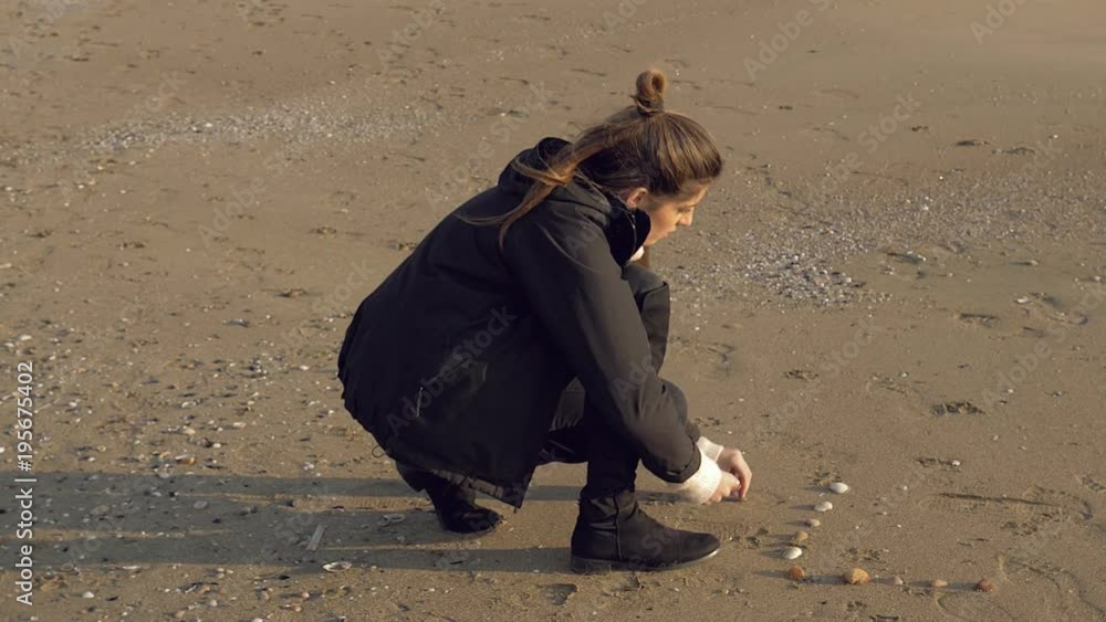 Beautiful woman on beach in winter making heart with seashell medium shot