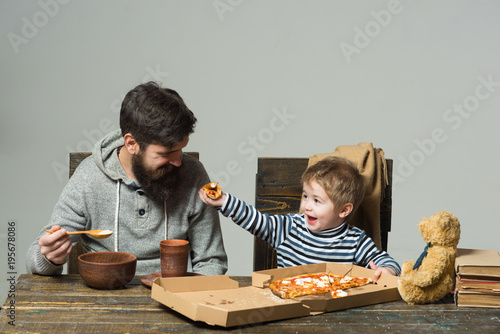 Happy father with child son eating pizza. Man and boy eating pizza at home party closeup. Friends eating pizza, having party at home, eating pizza and having fun. Family dinner with father photo