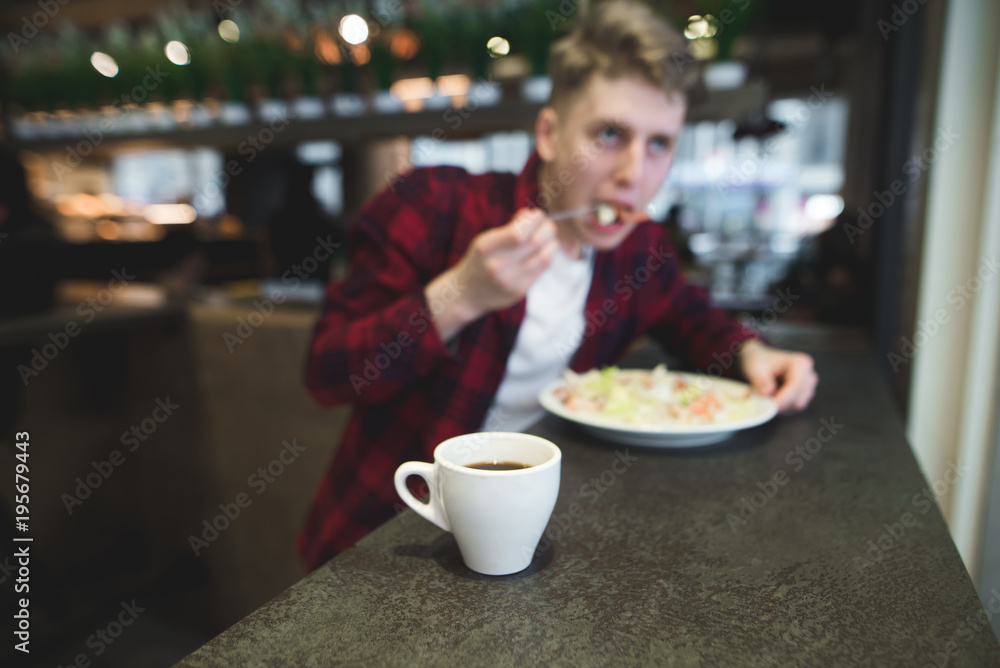 A cup of coffee on the background of a person who eats a restaurant. The cup is in focus, the person is blurred