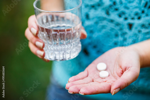 girl holds a glass of clean water and two white pills