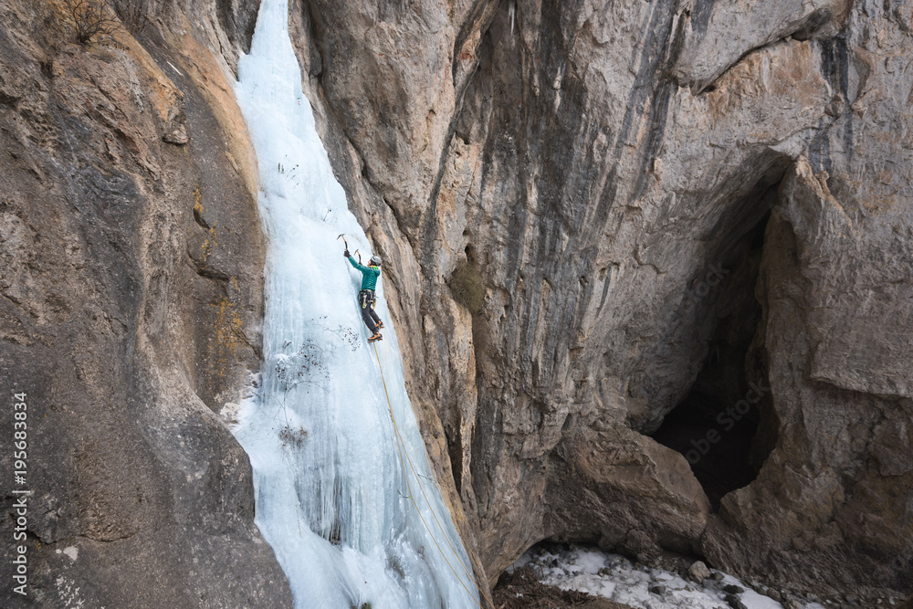 Man climbing on steep frozen waterfall using ice axes Man climbing on steep frozen waterfall using ice axes