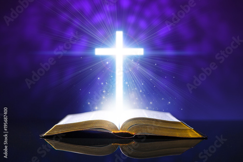Open bible on a glass desk with a glowing cross