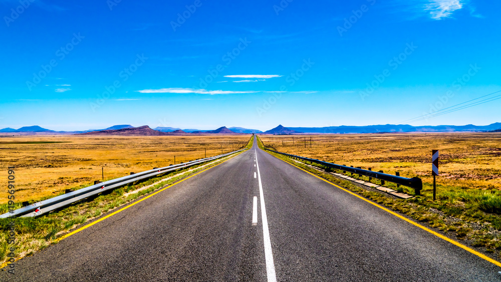 Long Straight Road through the Endless wide open landscape of the semi desert Karoo Region in Free State and Eastern Cape provinces in South Africa under blue sky