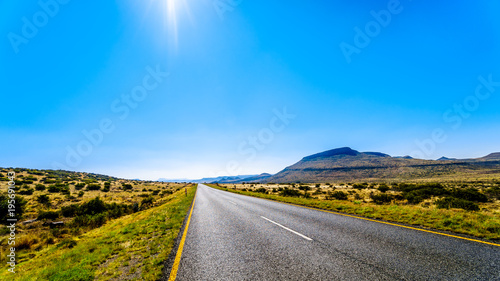 Long Straight Road through the Endless wide open landscape of the semi desert Karoo Region in Free State and Eastern Cape provinces in South Africa under blue sky