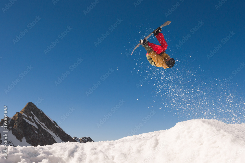 Male snowboarder doing extreme midair tricks against blue sky Male snowboarder doing extreme midair tricks against blue sky