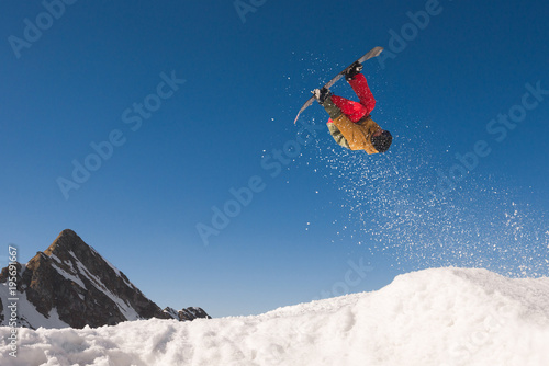 Male snowboarder doing extreme midair tricks against blue sky