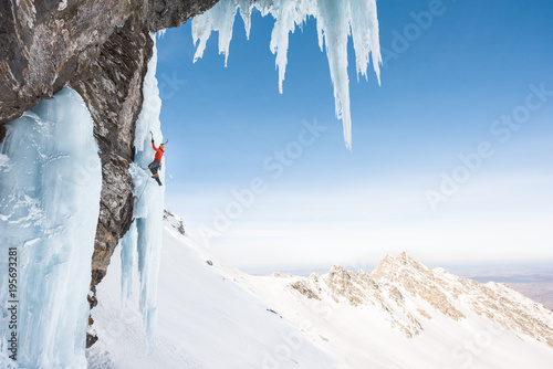 Anonymous man ice climbing on steep frozen waterfall in mountains photo