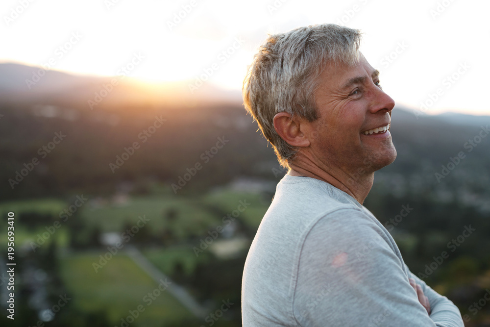 Content grey haired man smiling on hilltop at sunset Content grey haired man smiling on hilltop at sunset