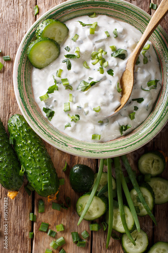 Homemade Indian raita dressing with herbs, spices and cucumber close-up in a bowl. Vertical top view