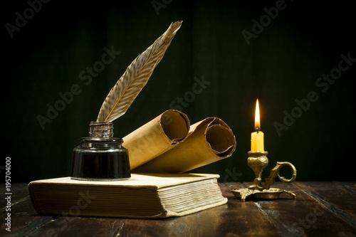 Education and writing concept, pen in ink bottle and candle holder with candle on wooden table.