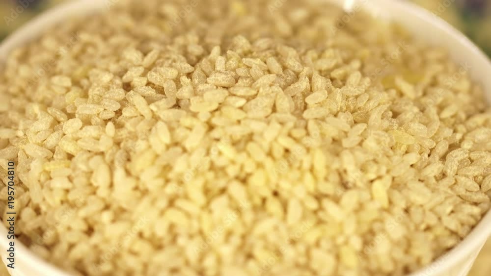 The plate from rice turns around itself on a support. Black background. White dry rice close up. Rice for pilaf. semi-indistinct shot The plate from rice turns around itself on a support. Black background. White dry rice close up. Rice for pilaf. semi-indistinct shot