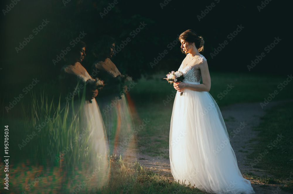 Young woman in a white dress is standing on the field. Portrait of girl outdoor. Romantic young woman posing on the background of sunset sky. Young woman in a white dress is standing on the field. Portrait of girl outdoor. Romantic young woman posing on the background of sunset sky.
