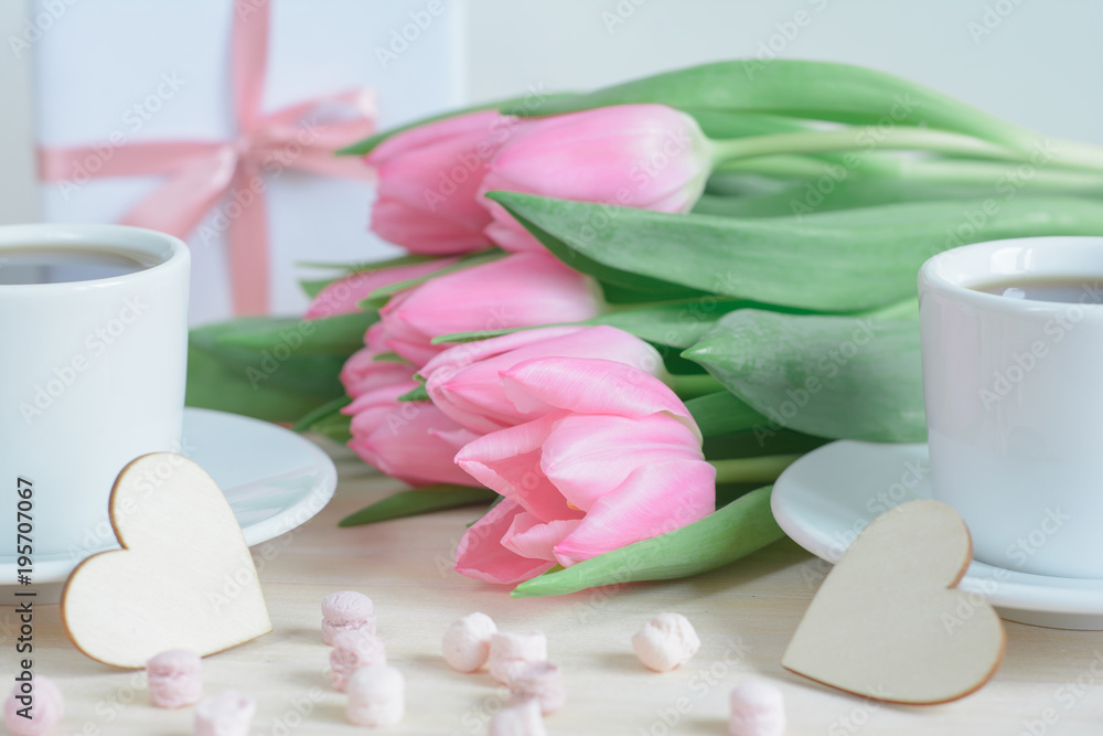 Romantic photo with pink tulips, two cups of coffee and wooden tiny hearts in the foreground