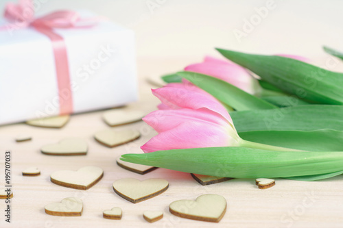 Fototapeta Naklejka Na Ścianę i Meble -  Light wooden desktop with wooden hearts, pink tulips and gift wrapped in white paper with satin ribbon