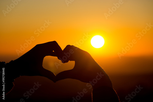 A heart hand gesture is silhouetted by the setting sun in Dartmoor, UK