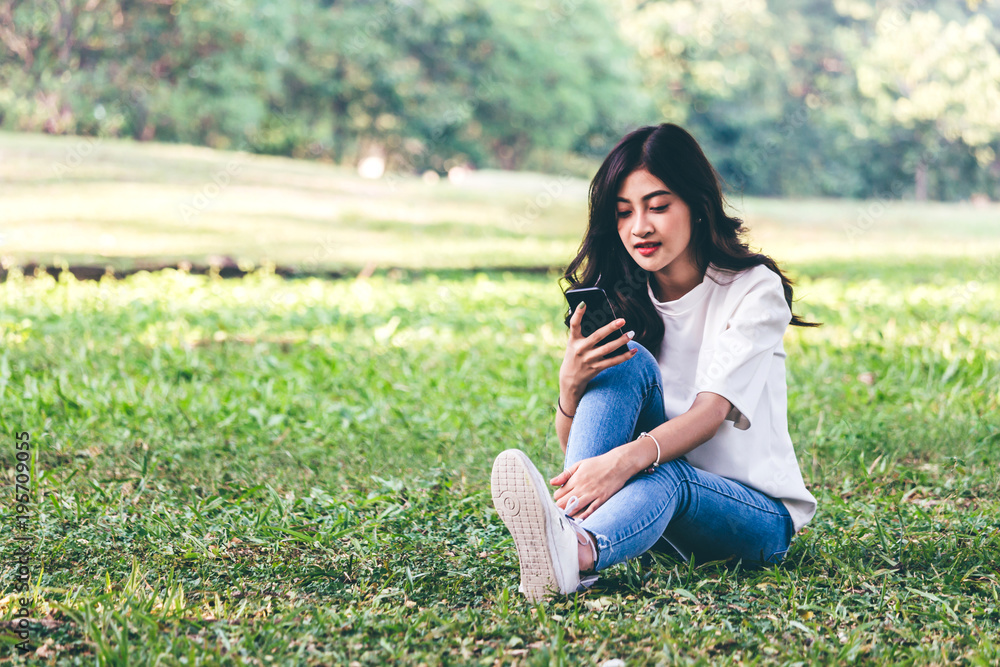 Woman relax and use smartphone sitting on grass in park Woman relax and use smartphone sitting on grass in park