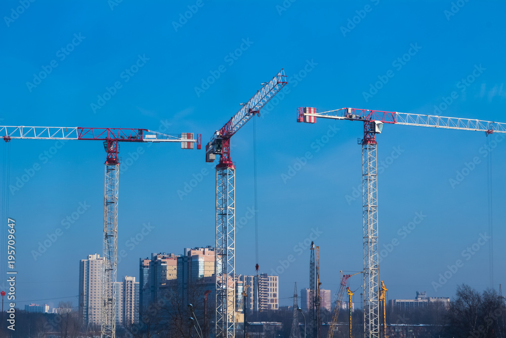 Three red industrial construction tower cranes build a house against the blue sky
