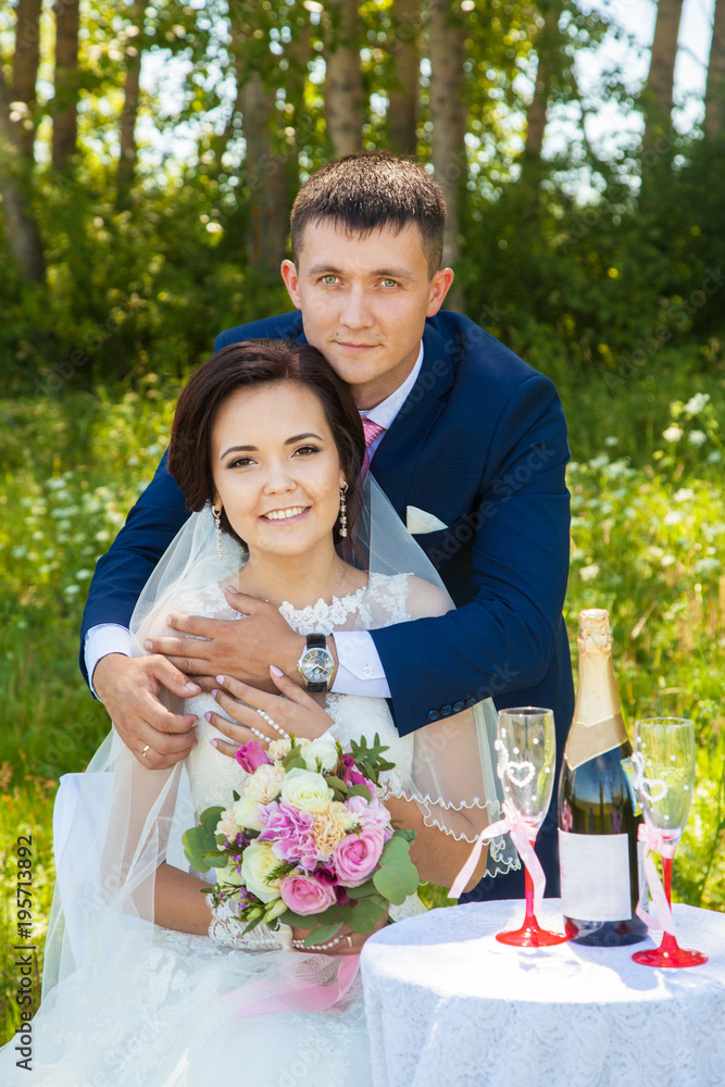 beautiful and happy newlyweds on a walk. summer wedding. Table with glasses and champagne beautiful and happy newlyweds on a walk. summer wedding. Table with glasses and champagne