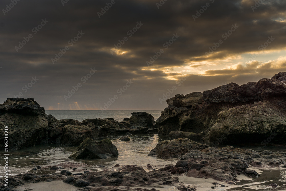 Sunset on the beach of Fuerteventura with lava rocks, dark clouds and small waves
