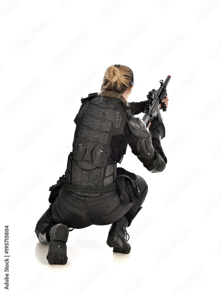 full length portrait of female soldier wearing black tactical armour, seated pose holding a gun, isolated on white studio background. full length portrait of female soldier wearing black tactical armour, seated pose holding a gun, isolated on white studio background.