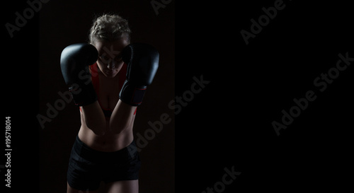 The beautiful young woman practices boxing. It costs in pose of protection against blow. Dark background.