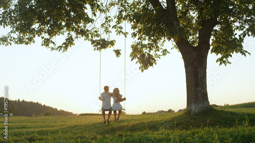LENS FLARE SILHOUETTE: Unrecognizable couple swaying on swing at golden twilight © helivideo