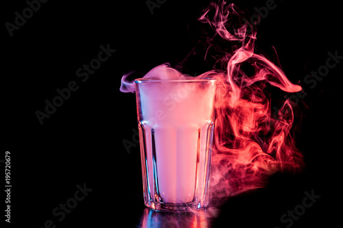 A  transparent  glass filled with a cloud from a red vape smokes and stands on a black isolated background