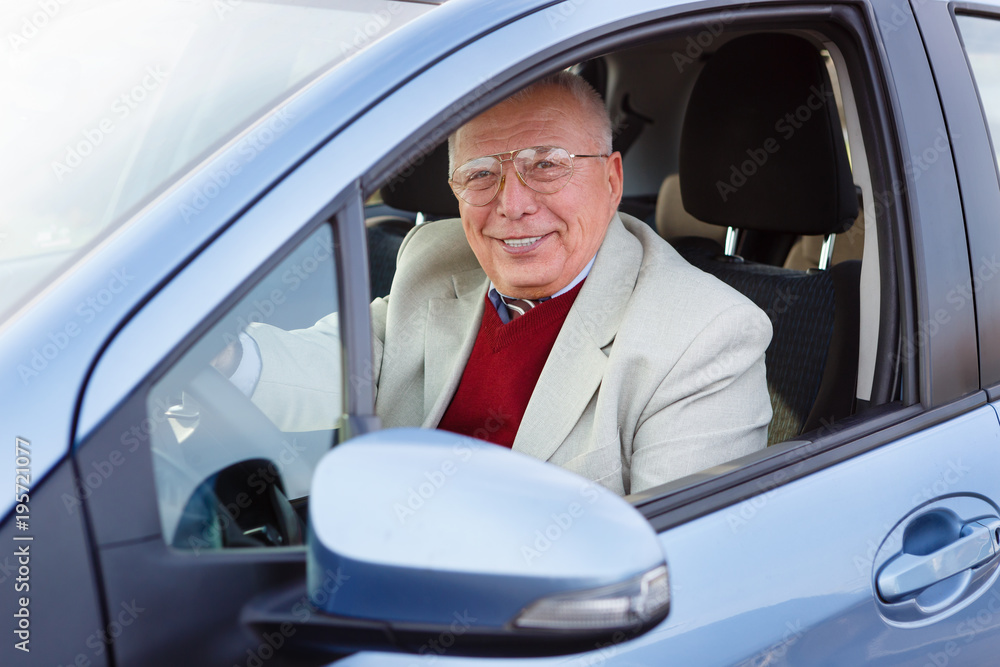 Old senior male 70-75 years old with goggles, sitting in car on driver seat and keeps the steering wheel. Spring and summer time, Happy and rich lifestyle concept