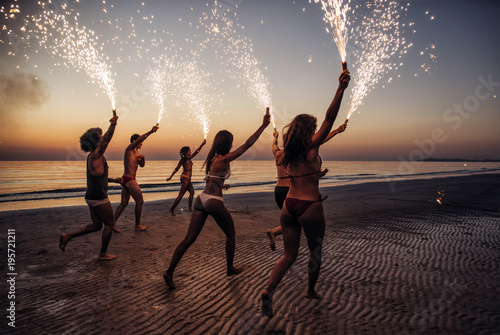 Group of friends having fun running on the beach with sparklers