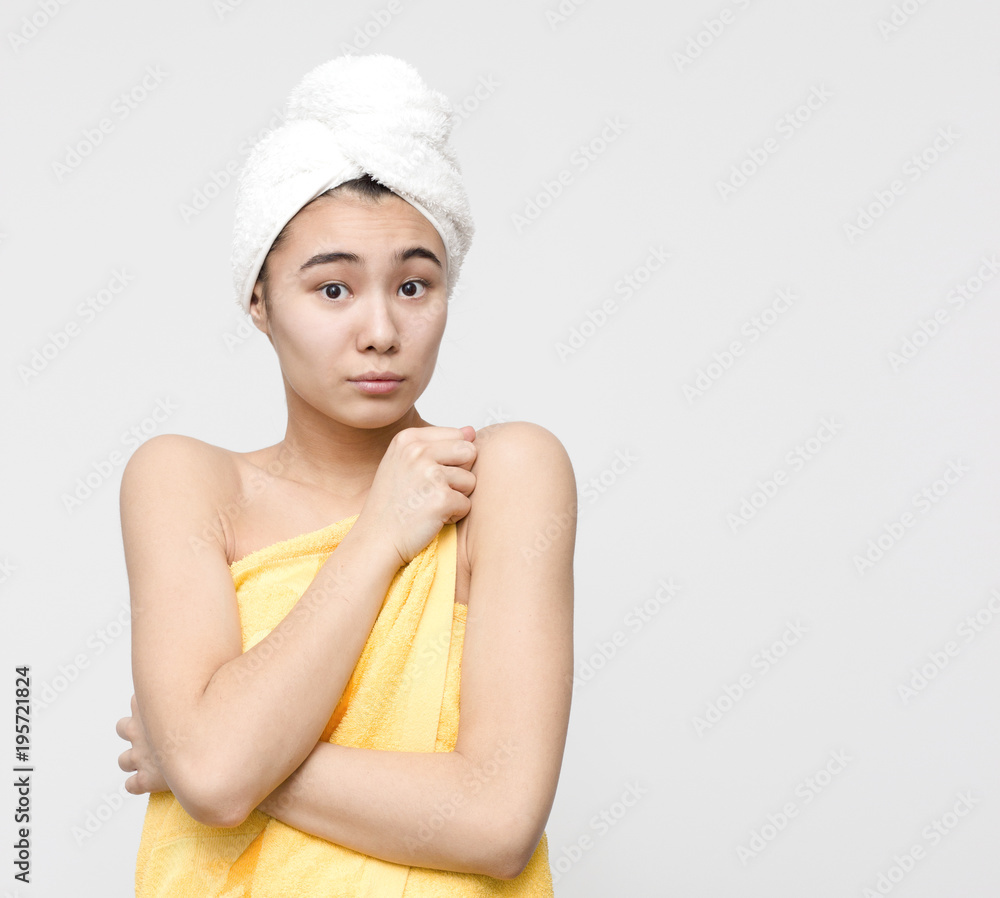 Indoor portrait of shy attractive asian woman holding her shoulders after shower wrapped in yellow towel on the white background. Beauty, skincare, bathroom and spa lifestyle concept Indoor portrait of shy attractive asian woman holding her shoulders after shower wrapped in yellow towel on the white background. Beauty, skincare, bathroom and spa lifestyle concept