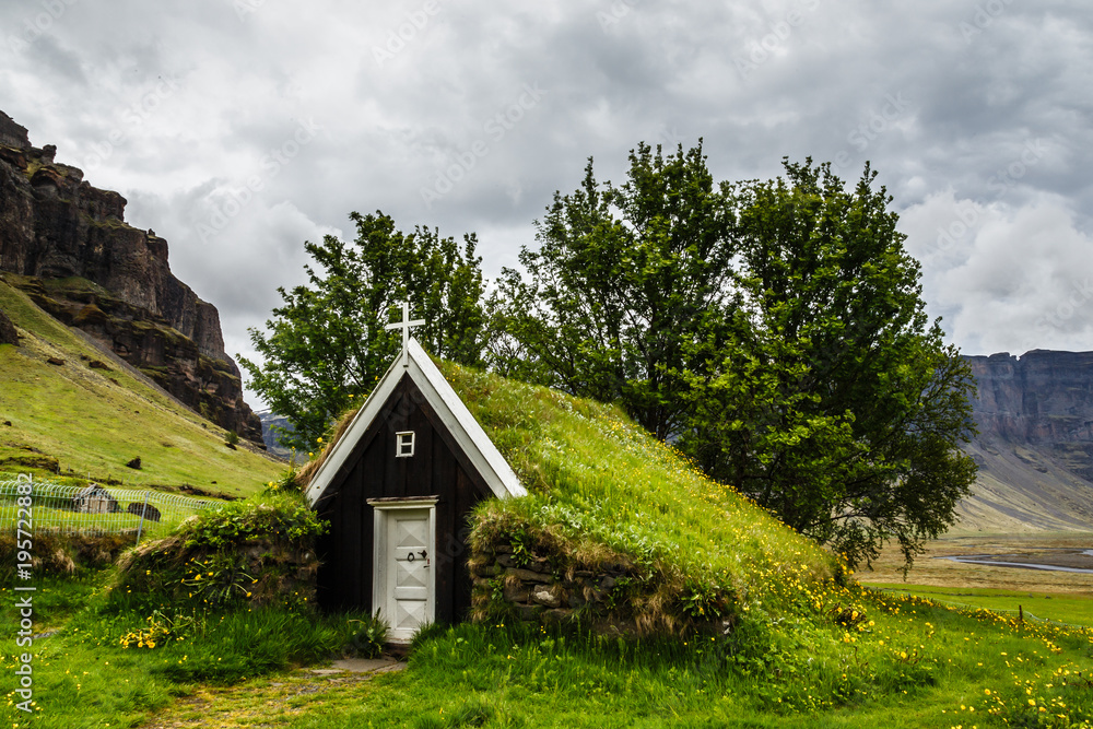 Icelandic traditional turf church covered with grass,  trees and rocks in the background near Kalfafell village, South Iceland
