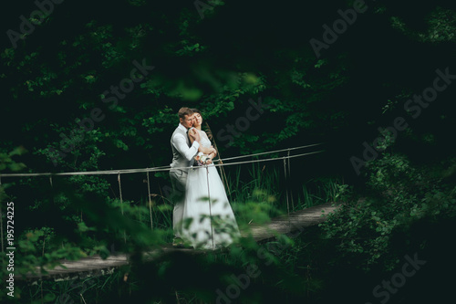 the bride and groom posing on a suspension bridge