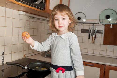 Little baby girl in gray dress fry egg in the kitchen