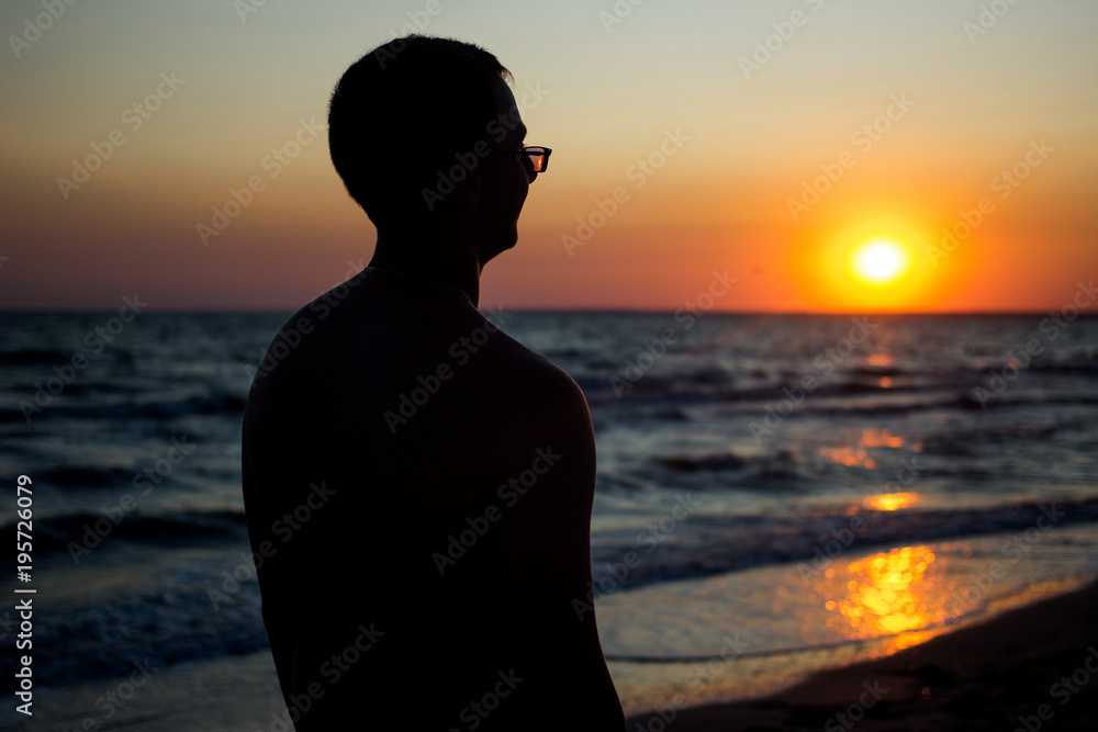 happy young man with glasses looks at sunset near the sea