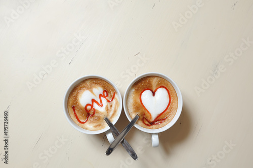 Two cups of coffee on the table with a picture of the heart and an inscription - love