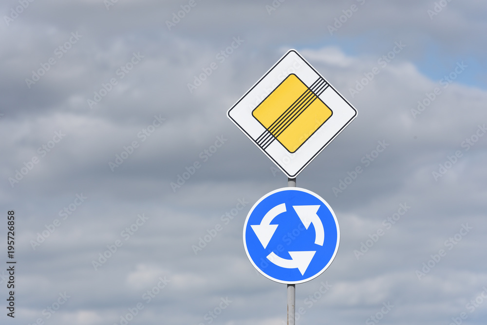 End of the main road and circular motion, roundabout sign, on the road against the sky with clouds End of the main road and circular motion, roundabout sign, on the road against the sky with clouds