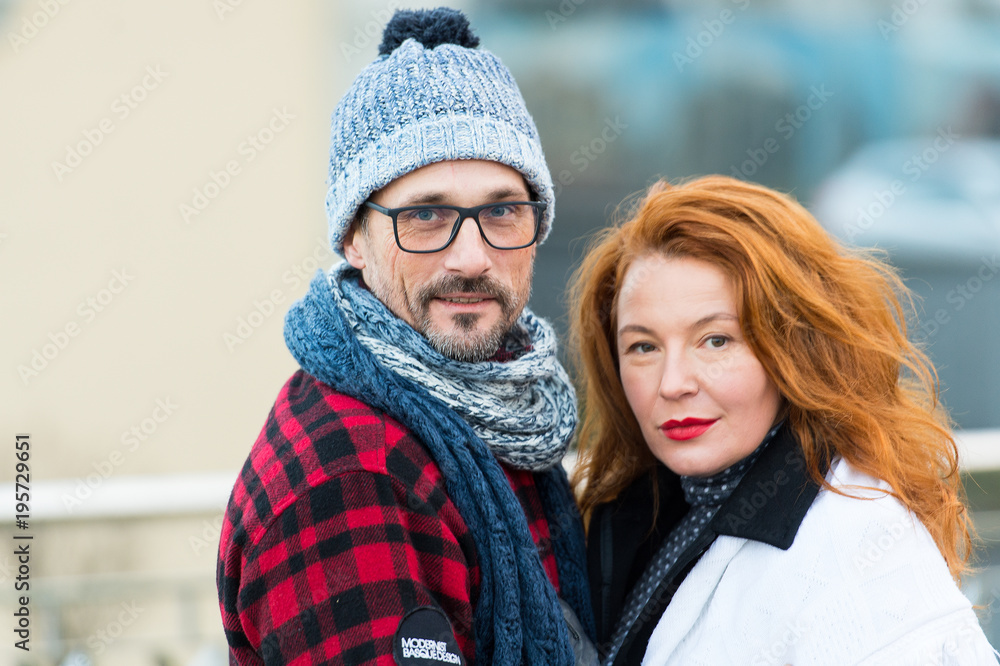 Portrait of sweet couple on street. Smiled man and happy woman posing for picture. Portrait of urban family. Red hair woman and gay in glasses hugging and looked to us
