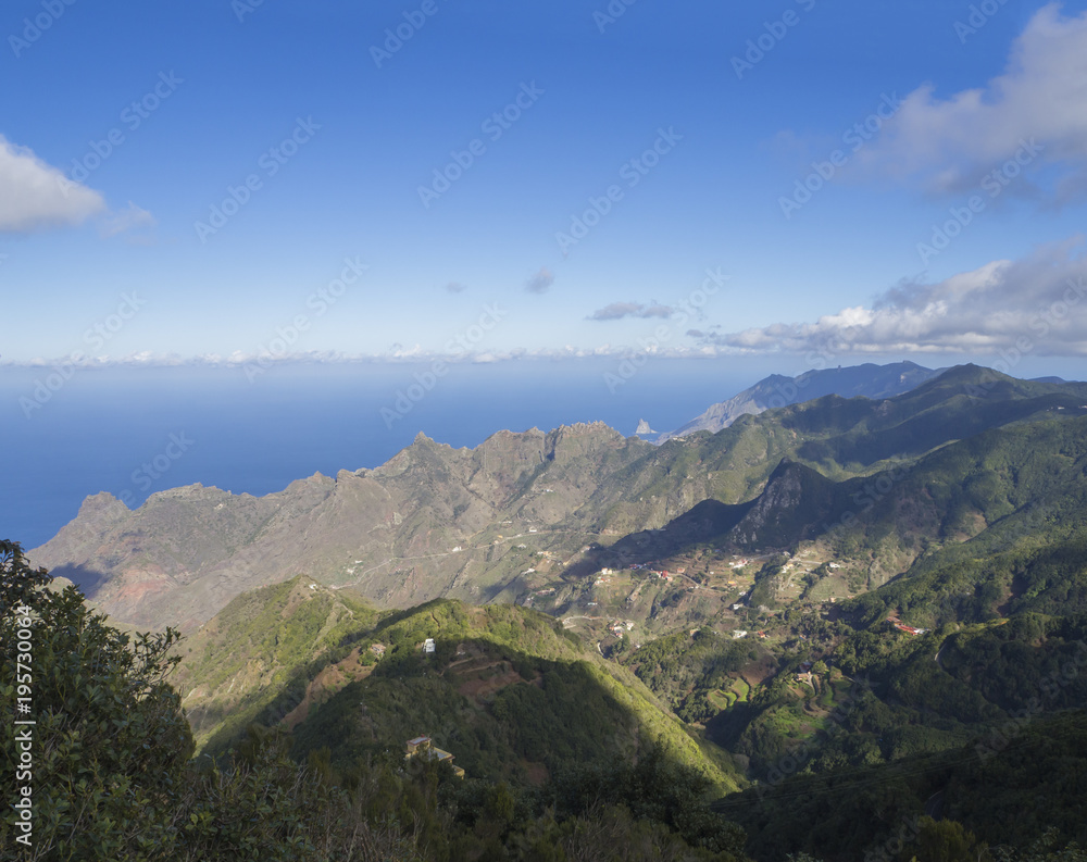 view point Amogoje, green hills with rock in the sea El Draguillo in anaga mountain, tenerife  canary island spain with dramatic blue sky white clouds background