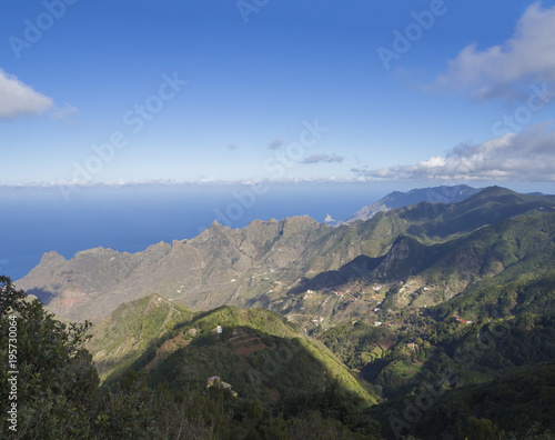 view point Amogoje, green hills with rock in the sea El Draguillo in anaga mountain, tenerife canary island spain with dramatic blue sky white clouds background