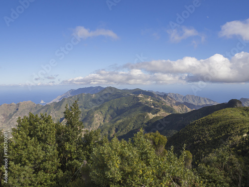 view point Amogoje, green hills with rock in the sea El Draguillo in anaga mountain, tenerife  canary island spain with dramatic blue sky white clouds background © Kristyna