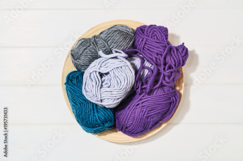 Top view of colorful knitting yarn balls and needlework accessories on white wooden textured table background. Photograph taken from above with copy space around products