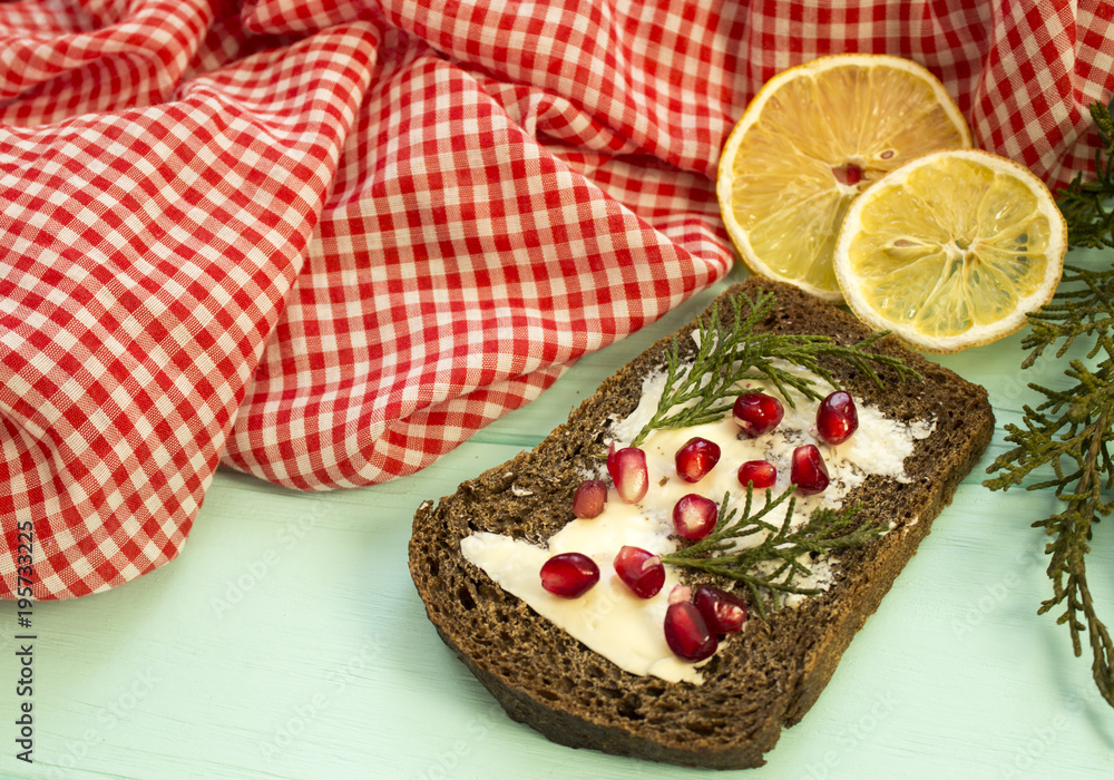 Black bread with grenades berries on turquoise wooden background. Christmas food, Christmas decorations with lemon, juniper, branch, red berries Black bread with grenades berries on turquoise wooden background. Christmas food, Christmas decorations with lemon, juniper, branch, red berries