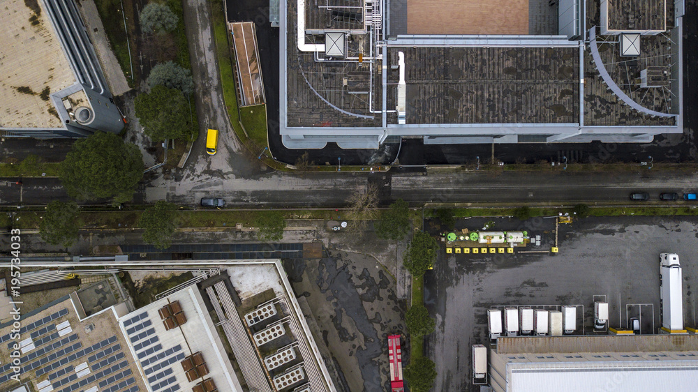 Obraz premium Perpendicular aerial view of a road in an industrial areaof a big city. Nobody is on the street. There are only a few cars, trucks and vans parked on the asphalt. The building is an office.