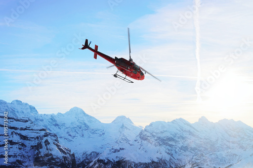 Fototapeta Naklejka Na Ścianę i Meble -  Red helicopter flying at Swiss Alps mountain Mannlichen winter sunset