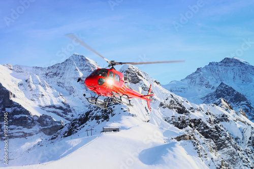 Red helicopter flying in winter Swiss Alps mountain under snow Mannlichen in winter photo