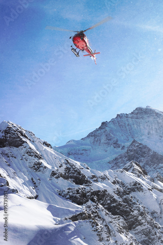 Red helicopter flying above Swiss Alpine mountain Mannlichen in winter