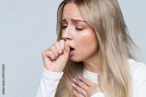 Photos Unhealthy young blonde woman coughing a lot, suffering with cough, has a chest pain, has flu symptom, isolated on gray background