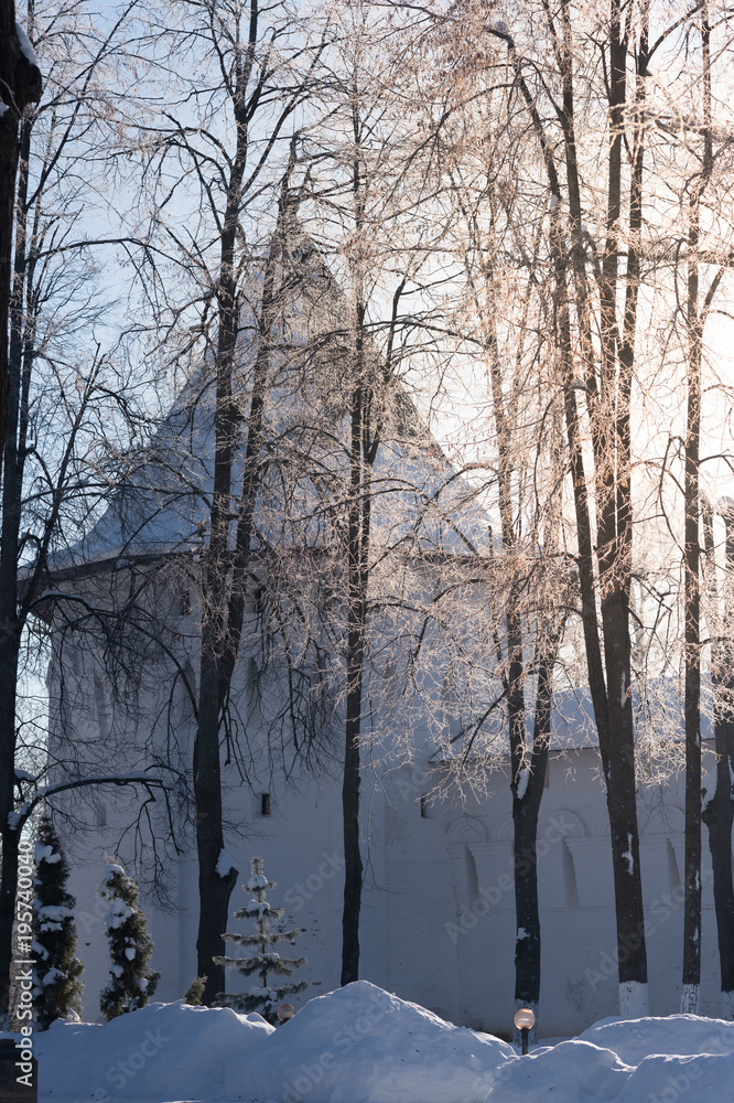 Tower of the white monastery wall in the snow. The sun shines through the frost on the trees. Monastery of St. Savva Storozhevsky in Zvenigorod near Moscow.