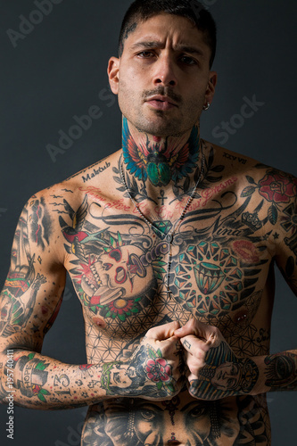 Handsome bare chested tattooed man portrait on grey background